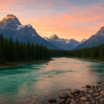 Weitwinkelaufnahme eines türkisfarbenen Flusses in den kanadischen Rocky Mountains bei Sonnenaufgang, umgeben von dichtem Nadelwald und schneebedeckten Gipfeln unter einem orange-rosa Himmel.