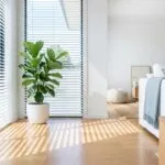 Helles Wohnzimmer mit halb geschlossenen Raffstores am Panoramafenster und Schatten auf dem Parkettboden.